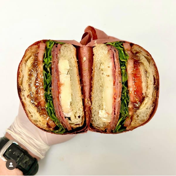 A Jholano’s Deli sandwich, cut in half, revealing layers of meat, cheese, lettuce, and tomato.