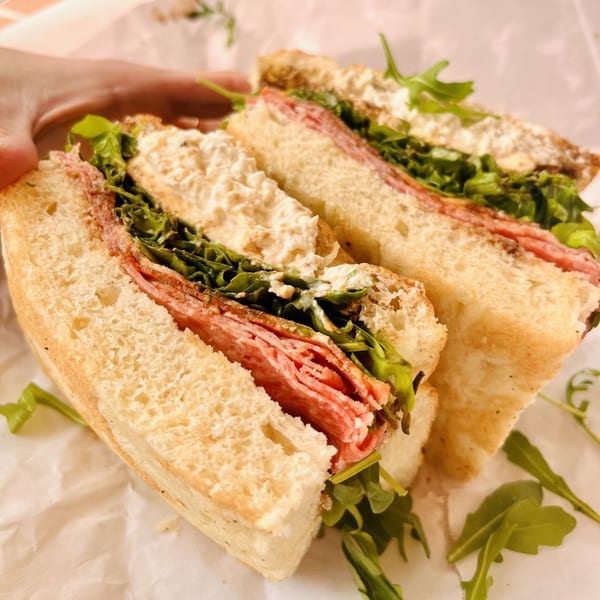 A Jholano's Deli sandwich, cut in half, revealing layers of meat, arugula, and creamy spread.