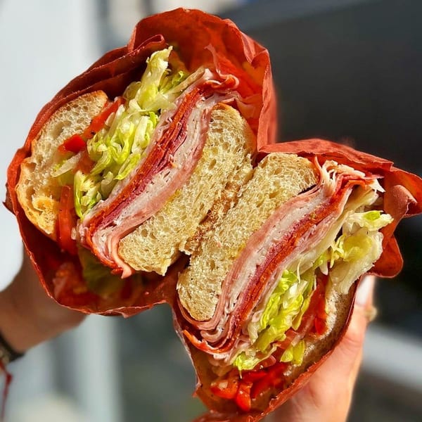 A Jholano's Deli sandwich, cut in half, revealing layers of meat, cheese, lettuce, and tomatoes.