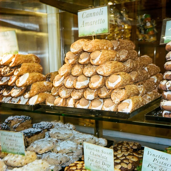 A display case filled with various Italian pastries, including cannoli and Venetian sweet almonds.