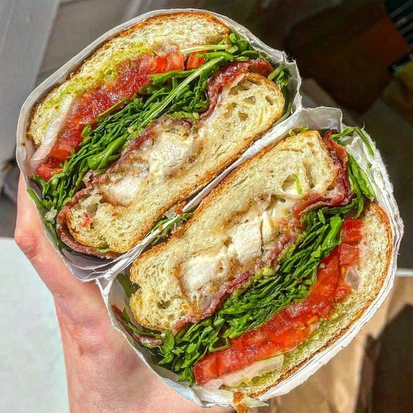 A Jholano’s Deli sandwich, cut in half, revealing chicken, bacon, lettuce, tomato, and sauce.