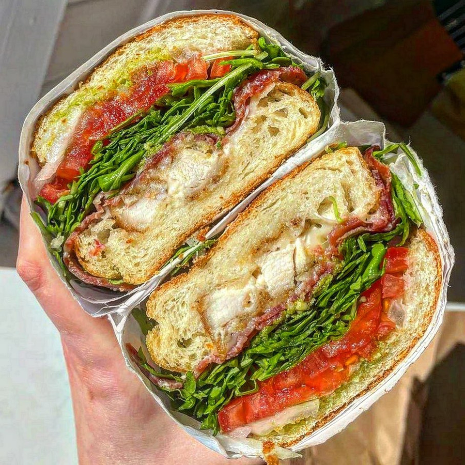 A Jholano’s Deli sandwich, cut in half, revealing chicken, bacon, lettuce, tomato, and sauce.