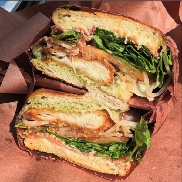 A Jholano’s Deli sandwich, cut in half, revealing fried chicken, lettuce, and sauce on ciabatta.