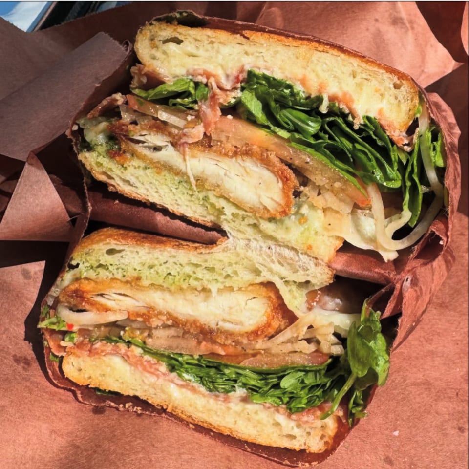 A Jholano's Deli sandwich, cut in half, revealing fried chicken, lettuce, and sauce on a baguette.